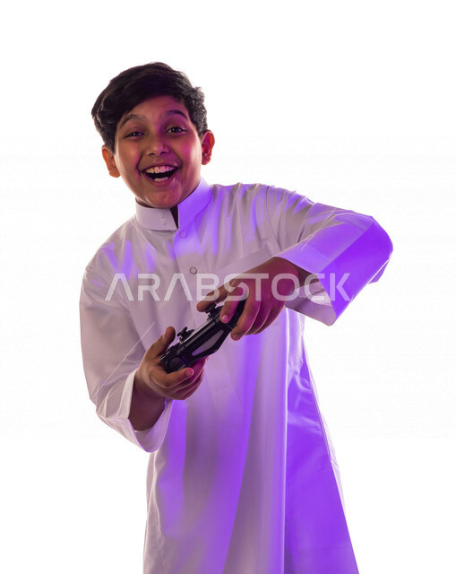 بورتريه لطفل عربي خليجي سعودي يرتدي الزي التقليدي ، يمسك بيده عصا التحكم و يلعب لعبة فيديو ، إيماءات و تعابير وجه  و يدين تدل على السعادة ، خلفية بيضاء
