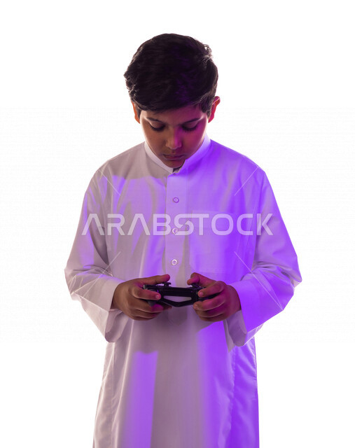 بورتريه لطفل عربي خليجي سعودي ، يمسك بيده عصا التحكم و يلعب بألعاب الفيديو ، المتعة و التسلية بألعاب الفيديو و ألعاب العالم الافتراضي ، ألعاب البلايستيشن الترفيهية ، تقنيات و ألعاب ، خلفية بيضاء