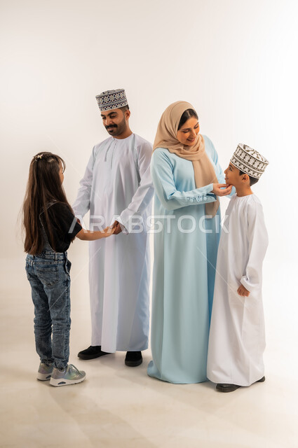 Caring and attention to children, exchanging dialogue and entertaining discussion, a family atmosphere full of affection, an Omani family spending a good time, the concept of a happy and connected family, a portrait of an Arab Gulf Omani man wearing a dishdasha and a kummah standing with his wife and children, full-length body, white background