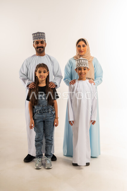 النظر إلى الكاميرا بايماءات السرور، عائلة عمانية تقضي وقت ممتع، مفهوم الأسرة السعيدة المترابطة، بورتريه لرجل عربي خليجي عماني يرتدي الدشداشة والكمة يقف مع زوجته وأبناءه، تعزيز العلاقات الاجتماعية، أجواء أسرية مليئة بالمودة, الجسم بالطول الكامل، خلفية بيضاء