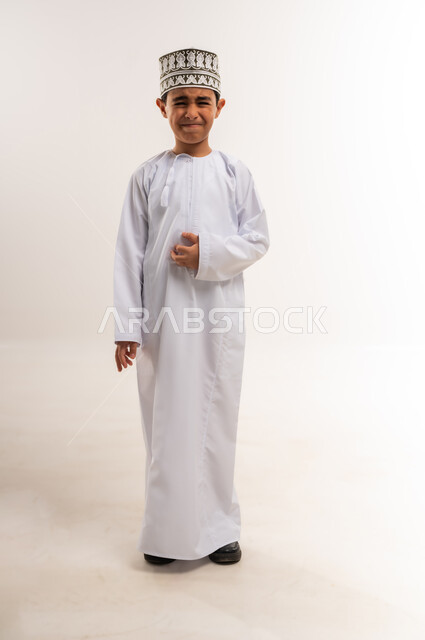 الحاجة للذهاب للطبيب ووضع خطة علاجية مناسبة، بورتريه لفتى عربي خليجي عماني يرتدي الدشداشة والكمة يضع يده على بطنه بإيماءات التألم الشديد، حالة إسعافية طارئة، آلام شديدة في المعدة، الإصابة بالمرض والتوعك, صورة الجسم بالطول الكامل, خلفية بيضاء