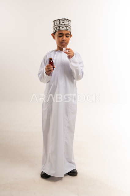 الالتزام باتخاذ الأدوية في الوقت المناسب لها, مفهوم الاستفادة من الدواء الموصوف, بورتريه لفتى عربي خليجي عماني يرتدي الدشداشة والكمة يحمل زجاج دواء عاتمة يرفع يده لشرب جرعة منه، الإصابة بالمرض والتوعك, صورة الجسم بالطول الكامل, خلفية بيضاء