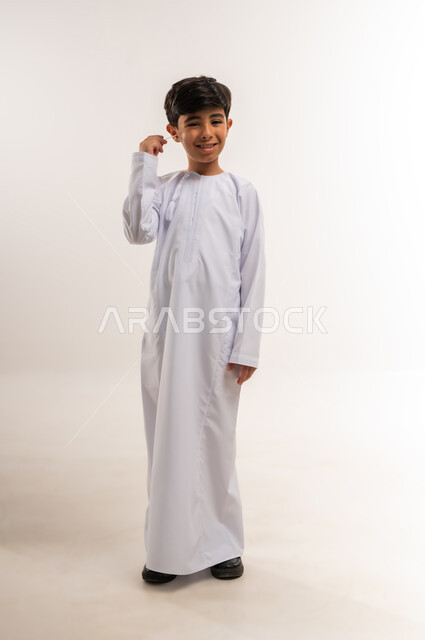 روتين نظافة الأذنين اليومية، العناية والاهتمام بصحة الأذن، استخدام أعواد ونكاشات القطن، بورتريه لفتى عربي خليجي عماني يرتدي الدشداشة يقوم وضع نكاشة قطنية داخل أذنه، الاهتمام المظهر الخارجي، الجسم بالطول الكامل، خلفية بيضاء