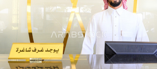 صورة مقربة لمكتب موظف إستقبال في الفندق السياحي ، سياحة وفندقة ، مكتب لخدمة العملاء ، مكتب إستقبال العملاء ، الحجز والإستفسار ، صورة مقربة لمكتب استقبال العملاء بلافتة يوجد غرف شاغرة ، رجل سعودي يرتدي الزي السعودي التقليدي