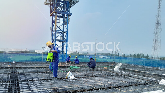 مفهوم الهندسة الانشائية والمعمارية، أعمال البناء وصب الخرسانات ووضع الأساسات الأولية، تنفيذ مخطط الإعمار وتشكيل الهيكل المعدني, مبنى قيد الإنشاء والتشييد في المملكة العربية السعودية, عمال عرب خليجيون سعوديون يرتدون سترة وخوذة الحماية يعملون في موقع البناء