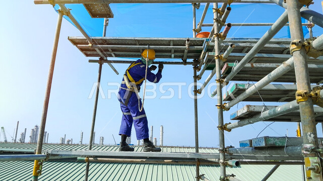 أعمال البناء وصب الخرسانات ووضع الأساسات الأولية، تنفيذ مخطط الإعمار وتشكيل الهيكل المعدني, مبنى قيد الإنشاء والتشييد في المملكة العربية السعودية, عامل عربي خليجي سعودي يرتدي سترة وخوذة الحماية يقوم بوضع السقالة, مفهوم الهندسة الانشائية والمعمارية
