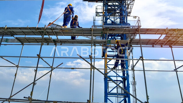 High scaffolding construction, structural and architectural engineering concept, concrete pouring and laying of initial foundations, implementation of construction plan and forming of metal structure, two Saudi Arabian Gulf workers doing construction work