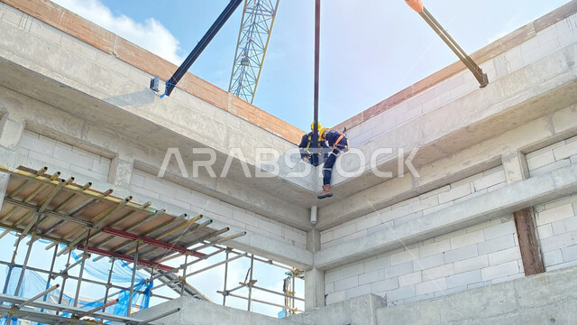 الإعمار وتنفيذ المخطط المعماري, مبنى قيد الإنشاء والتشييد, صب الخرسانات ووضع الأساسات الأولية, مفهوم الهندسة الانشائية والمعمارية, عاملان عربيان خليجيان سعوديان يرتديان سترة وخوذة الحماية يقومون بأعمال البناء