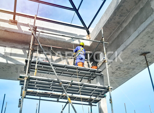 Laying the initial foundations, implementing the construction plan and forming the metal structure, a building under construction and erection in the Kingdom of Saudi Arabia, a Saudi Arabian Gulf worker wearing a protective jacket and helmet is placing the high scaffolding, the concept of structural and architectural engineering
