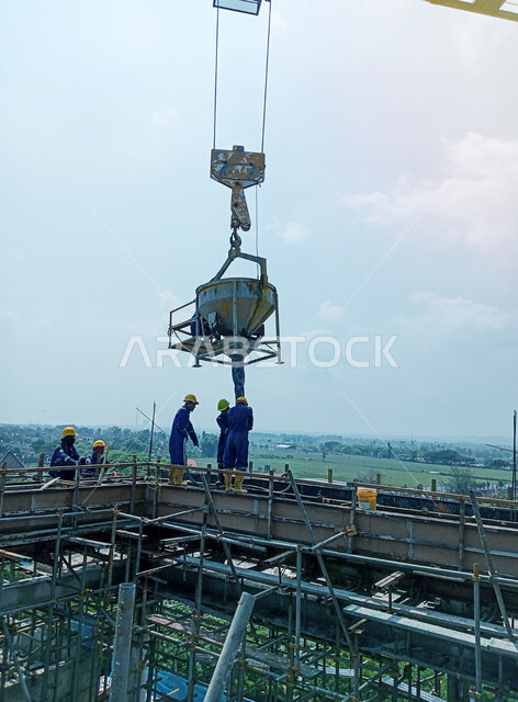 أعمال التشييد والبناء في السعودية, إنشاء الأساسات ووضع الخرسانات, مفهوم الهندسة الانشائية والمعمارية, تنفيذ مخطط الإعمار, عمال عرب خليجيون سعوديون يرتدون خوذة الحماية يقومون برفع دلو الخرسانة