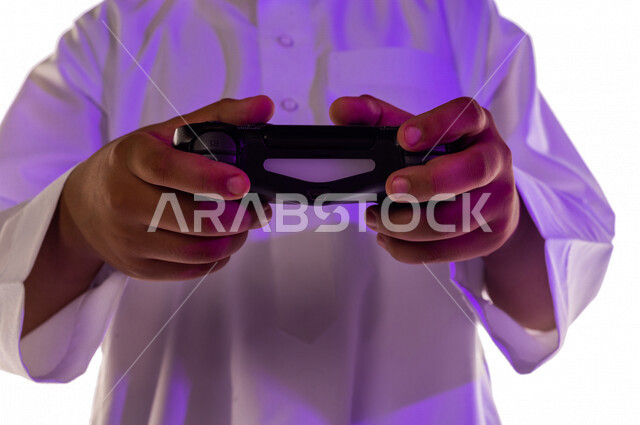 بورتريه لطفل عربي خليجي سعودي ، يمسك بيده عصا التحكم و يلعب بألعاب الفيديو ، المتعة و التسلية بألعاب الفيديو و ألعاب العالم الافتراضي ، ألعاب البلايستيشن الترفيهية ، تقنيات و ألعاب ، خلفية بيضاء