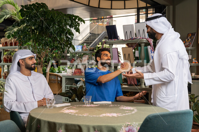 التسلية والترفيه في العطلة، رجل عربي خليجي اماراتي يرتدي الكندورة والغترة البيضاء يقوم بالقاء التحية والسلام على اصدقائه في المقهى، قضاء وقت ممتع ومسلي مع الأصدقاء في الخارج، الكافيهات والمطاعم في الامارات العربية المتحدة