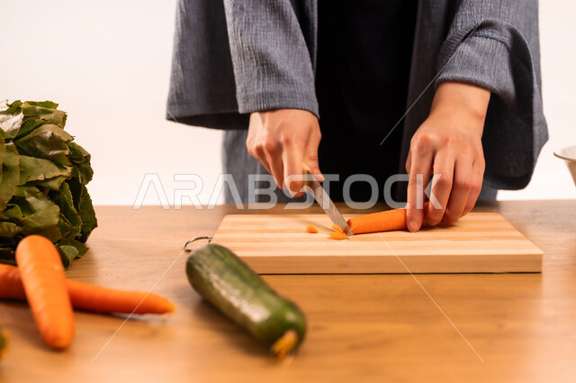 Diet concept, preparing delicious recipes, close-up portrait of veiled Saudi Arabian Gulf woman's hands cutting vegetables, a group of fresh vegetables, preparing salads and healthy dishes, housewife's task and responsibility, white background