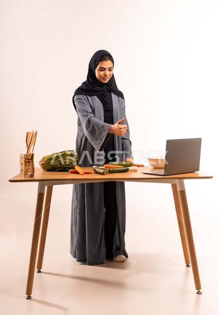 تعابير القبول والرضا، إعداد السلطة والأطباق الصحية، مفهوم النظام الغذائي، استخدام الحاسوب المحمول، بورتريه لامرأة عربية خليجية سعودية محجبة ترفع إصبع الإبهام بايماءات الاعجاب، مجموعة من الخضراوات الطازجة، مشاركة تحضير الوصفات على مواقع التواصل الاجتماعي، صورة لكامل الجسم، خلفية بيضاء