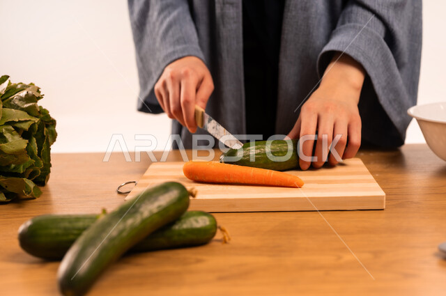 تحضير الوصفات اللذيذة، مفهوم النظام الغذائي، بورتريه مقرب لايدي امرأة عربية خليجية سعودية محجبة تقوم بتقطيع الخضار، مجموعة من الخضراوات الطازجة، إعداد السلطات والأطباق الصحية، مهمة ومسؤولية ربة المنزل، خلفية بيضاء