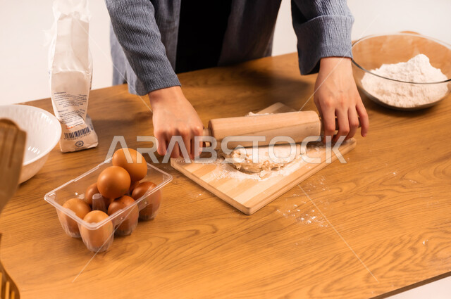 إعداد المخبوزات والمعجنات الشهية، تجهيز المكونات لصناعة الخبز، استخدام أداة فرد العجين، بورتريه مقرب لايدي امرأة عربية خليجية سعودية محجبة تحمل بيدها الشوبك (النشابة) تقوم بتحضير الطعام، أدوات خاصة بالمطبخ، مسؤولية ربة المنزل، خلفية بيضاء