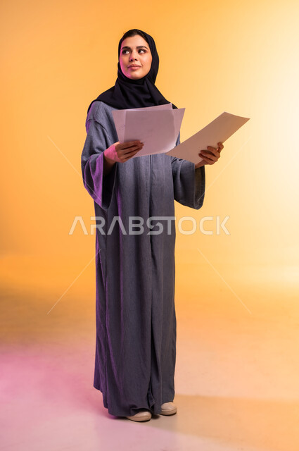 النظر إلى مكان ما،  اعداد التقارير الخاصة بالعمل، بورتريه لامرأة عربية خليجية سعودية محجبة ترتدي العباءة تحمل بيدها مجموعة من الأوراق بيضاء، مراجعة ومتابعة الخطط والمشاريع، تبادل الخبرات والمهارات، الجسم بالطول الكامل، خلفية ملونة