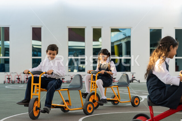 قضاء وقت ممتع في النشاط الترفيهي في مدارس الإمارات العربية المتحدة، سباقات وفعاليات متميزة، ركوب الدراجة ثلاثية العجلات بتعابير الفرح والسرور، مجموعة من الطلاب العرب الخليجيين الاماراتيين يلعبون على الدراجات أثناء الفسحة في المدرسة