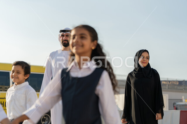 الاستعداد لبدء العام الدراسي الجديد بتعابير السرور، الحضور المبكر للحصص، الحافلة المدرسية الصفراء، موسم العودة إلى المدارس في الامارات، إعطاء الدعم النفسي والتحفيز المعنوي للطلاب، معلم ومعلمة عربيان خليجيان اماراتيان يدخلان الى المدرسة مع الطلاب