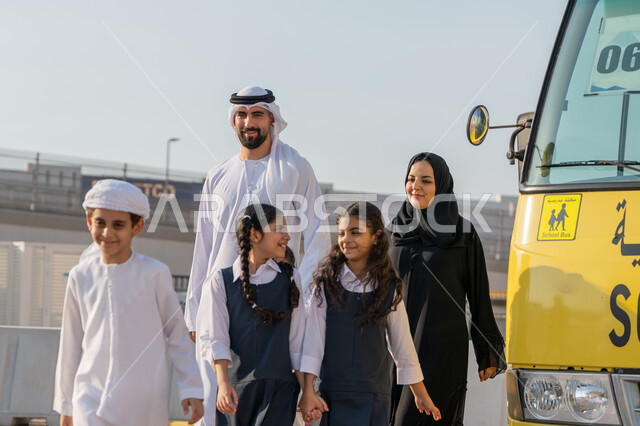 Yellow school bus, back to school season in the Emirates, preparing to start the new school year with expressions of joy, early attendance at classes, providing psychological support and moral motivation to students, two Emirati Gulf Arab teachers entering the school with the students