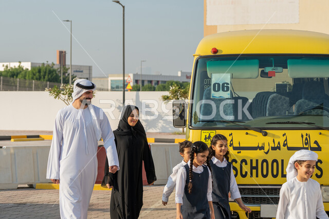 موسم العودة إلى المدارس في الامارات، الاستعداد لبدء العام الدراسي الجديد بتعابير السرور، الحضور المبكر للحصص، إعطاء الدعم النفسي والتحفيز المعنوي للطلاب، معلم ومعلمة عربيان خليجيان اماراتيان يدخلان الى المدرسة مع الطلاب، الحافلة المدرسية الصفراء