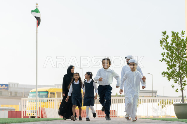 الاستعداد لبدء العام الدراسي الجديد بتعابير السرور، الحضور المبكر للحصص، إعطاء الدعم النفسي والتحفيز المعنوي للطلاب، موسم العودة إلى المدارس في الامارات، معلم ومعلمة عربيان خليجيان اماراتيان يدخلان الى المدرسة مع الطلاب، الحافلة المدرسية الصفراء