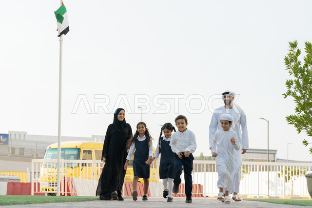 الحضور المبكر للحصص، الاستعداد لبدء العام الدراسي الجديد بتعابير السرور، إعطاء الدعم النفسي والتحفيز المعنوي للطلاب، موسم العودة إلى المدارس في الامارات، معلم عربي خليجي اماراتي يرتدي الكندورة و الغترة يدخل الى المدرسة مع الطلاب، الحافلة المدرسية الصفراء