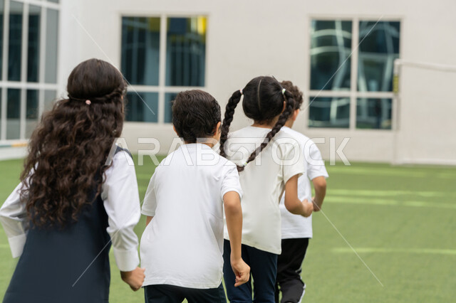 نشاط و فعالية ترفيهية للأولاد في مدارس الامارات العربية المتحدة, أجواء مليئة بالمرح والتفاعل الإيجابي, صورة من الخلف لمجموعه من الطلاب العربيين الخليجيين الاماراتيين يقومون بممارسة رياضة الجري في الهواء الطلق في باحة المدرسة