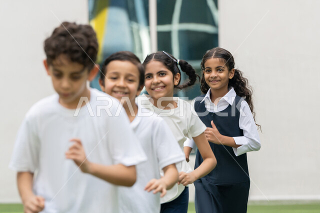 أجواء مليئة بالمرح والتفاعل الإيجابي, تمرين الإحماء والاستعداد، صورة مقربة لمجموعه من الطلاب العربيين الخليجيين الاماراتيين يقومون بممارسة رياضة الجري في الهواء الطلق بتعابير الفرح و السرور في باحة المدرسة, نشاط و فعالية ترفيهية للأولاد في مدارس الامارات