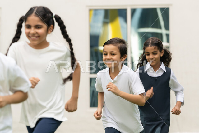 تمرين الإحماء والاستعداد، أجواء مليئة بالمرح والتفاعل الإيجابي, صورة مقربة لمجموعه من الطلاب العربيين الخليجيين الاماراتيين يقومون بممارسة رياضة الجري في الهواء الطلق بتعابير الفرح و السرور في باحة المدرسة, نشاط و فعالية ترفيهية للأولاد في مدارس الامارات