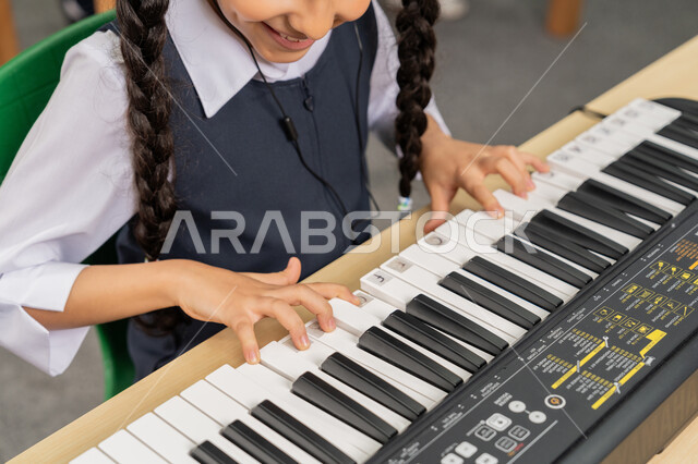 تنمية الموهبة والقدرة الموسيقية في الإمارات العربية المتحدة، صورة مقربة لفتاة عربية خليجية اماراتية تقوم بتعلم العزف على آلة البيانو بإيماءات السرور والسعادة في حصة الموسيقى، قضاء وقت ممتع بالنشاط الترفيهي، ممارسة الهواية المفضلة
