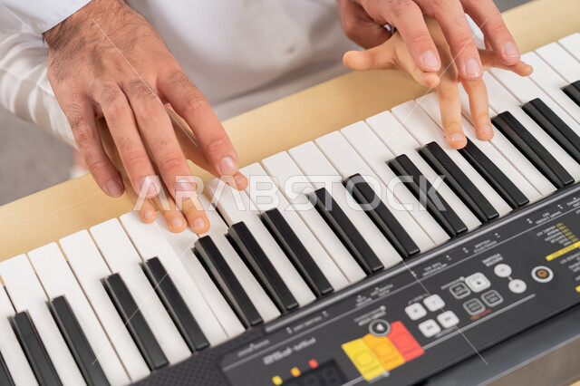 اب يقوم بتعليم ابنه العزف على البيانو، ممارسة الهوايه المفضله وتنمية القدرات الموسيقيه، قضاء وقت ممتع بالنشاط الترفيهي الموسيقي في المدرسه، صورة مقربه لايدي معلم عربي اماراتي خليجي يساعد التلميذ في حصة الموسيقى