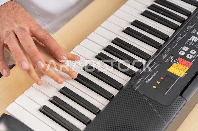 تنمية المهارات والقدرات الموسيقية، قضاء وقت ممتع بالأنشطة الترفيهية في مدارس الإمارات العربية المتحدة، صورة مقربة من الاعلى لايدي مدرس عربي خليجي اماراتي يقوم بمساعدة تلميذه في العزف على البيانو، اب يقوم بتعليم ابنه على ممارسة هوايته المفضلة