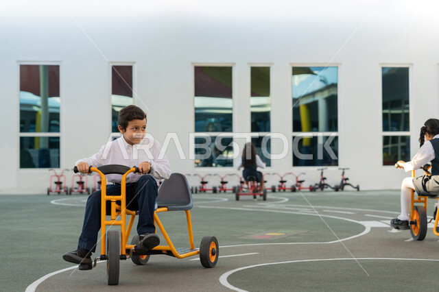 Having a great time with recreational activities in UAE schools, special races and events, riding a tricycle with expressions of joy and happiness, a group of Emirati Gulf Arab students playing on bikes during recess at school