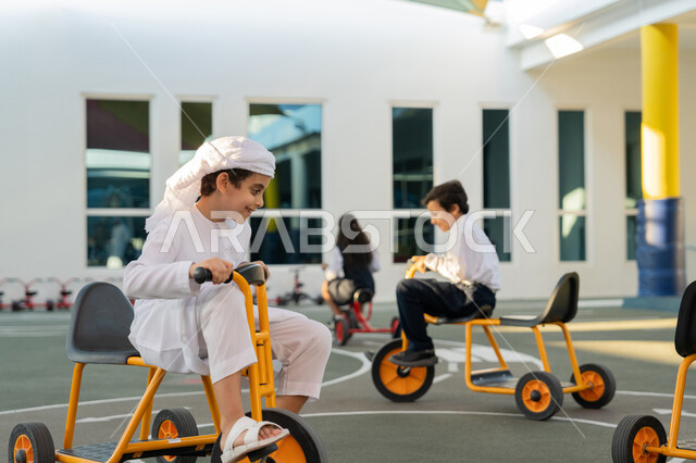 سباق وفعالية متميزة، ركوب الدراجة ثلاثية العجلات بتعابير الفرح والسرور، مجموعة من الطلاب العرب الخليجيين الاماراتيين يلعبون على الدراجات أثناء الفسحة في المدرسة، قضاء وقت ممتع في النشاط الترفيهي في مدارس الإمارات العربية المتحدة