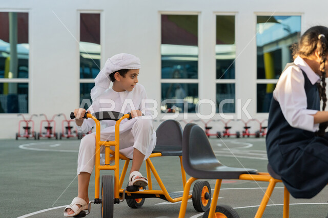 ركوب الدراجة ثلاثية العجلات بتعابير الفرح والسرور، مجموعة من الطلاب العرب الخليجيين الاماراتيين يلعبون على الدراجات أثناء الفسحة في المدرسة، سباق وفعالية متميزة، قضاء وقت ممتع في النشاط الترفيهي في مدارس الإمارات العربية المتحدة