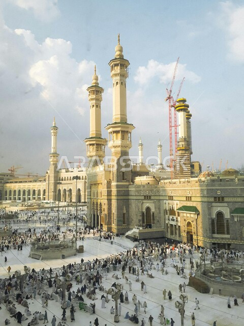 المعتمرين والحجاج في الساحات الخارجية للمسجد الحرام في مكة المكرمة، الحرم المكي الشريف في المملكة العربية السعودية في النهار، أداء مناسك الحج والعمرة، العبادة والتقرب إلى الله، المعالم الدينية الاسلامية المقدسة
