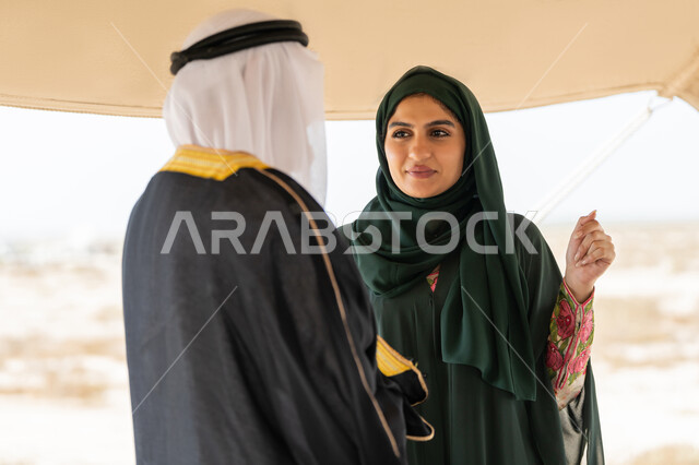 ايماءات السعادة والسرور والاعتزاز، تبادل الاحاديث وزيارة الاماكن التاريخية القديمة، ذكرى اليوم الوطني الاماراتي 1971، الاحتفال بتأسيس الاتحاد 2 ديسمبر، رجل عربي خليجي إماراتي يرتدي الكندورة والغترة والبشت يقف مع إمراة ترتدي العباءة والحجاب داخل خيمة في الصحراء