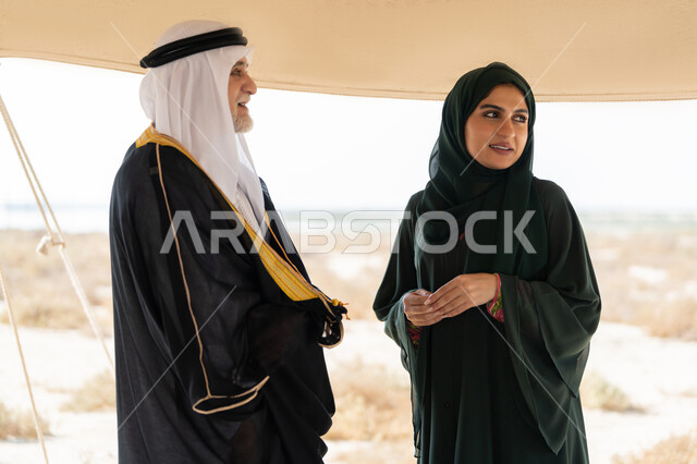 ايماءات السعادة والسرور والاعتزاز، تبادل الاحاديث وزيارة الاماكن التاريخية القديمة، ذكرى اليوم الوطني الاماراتي 1971، الاحتفال بتأسيس الاتحاد 2 ديسمبر، رجل عربي خليجي إماراتي يرتدي الكندورة والغترة والبشت يقف مع إمراة ترتدي العباءة والحجاب داخل خيمة في الصحراء