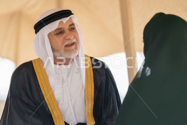 Founding of the Union December 2, Close-up of an Emirati Gulf Arab man wearing a kandura, ghutra and bisht standing with a woman wearing an abaya and hijab inside a tent in the desert, gestures of happiness, pleasure and pride, exchanging conversations and visiting ancient historical places, the memory of the UAE National Day 1971