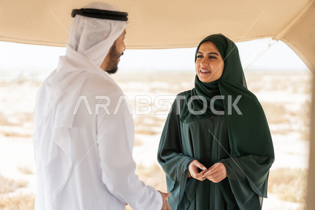 تبادل الاحاديث وزيارة الاماكن التاريخية القديمة، ذكرى اليوم الوطني الاماراتي 1971، الاحتفال بتأسيس الاتحاد 2 ديسمبر، شاب عربي خليجي إماراتي يرتدي الكندورة والغترة البيضاء يقف مع إمراة ترتدي العباءة والحجاب داخل خيمة في الصحراء، تعابير السعادة والسرور والاعتزاز