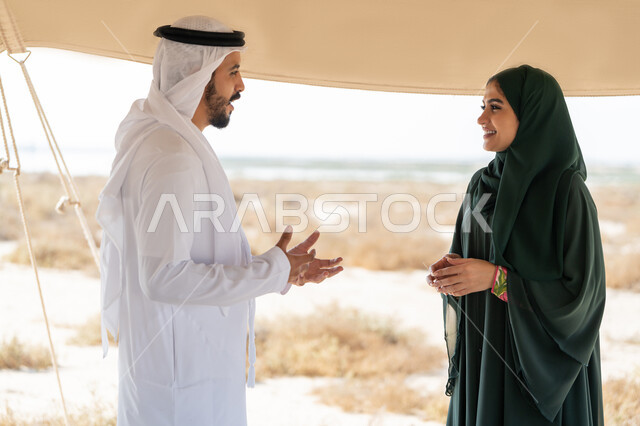 تعابير السعادة والسرور والاعتزاز، تبادل الاحاديث وزيارة الاماكن التاريخية القديمة، ذكرى اليوم الوطني الاماراتي 1971، الاحتفال بتأسيس الاتحاد 2 ديسمبر، شاب عربي خليجي إماراتي يرتدي الكندورة والغترة البيضاء يقف مع إمراة ترتدي العباءة والحجاب داخل خيمة في الصحراء
