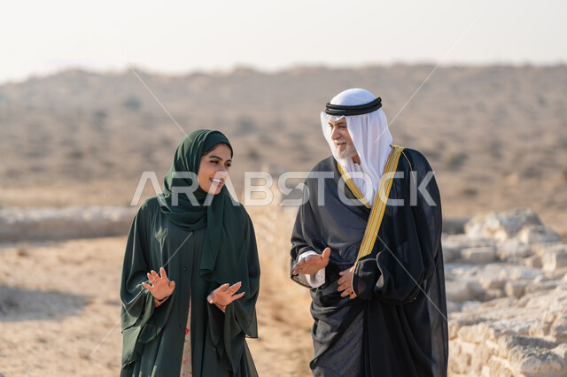 اليوم الوطني الاماراتي 1971، تأسيس الاتحاد 2 ديسمبر، رجل عربي خليجي إماراتي يرتدي الكندورة والغترة والبشت يتجول مع إمراة ترتدي العباءة والحجاب في الصحراء الاماراتية، تعابير وايماءات الفخر والاعتزاز وحب الوطن، تبادل الاحاديث وزيارة الاماكن التاريخية القديمة
