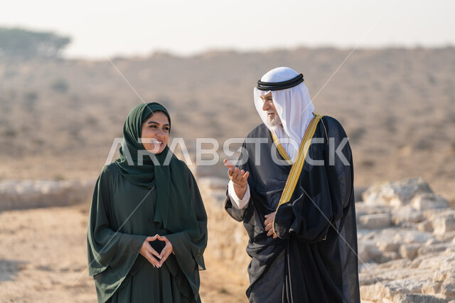 اليوم الوطني الاماراتي 1971، تأسيس الاتحاد 2 ديسمبر، رجل عربي خليجي إماراتي يرتدي الكندورة والغترة والبشت يتجول مع إمراة ترتدي العباءة والحجاب في الصحراء الاماراتية، تعابير وايماءات الفخر والاعتزاز وحب الوطن، تبادل الاحاديث وزيارة الاماكن التاريخية القديمة