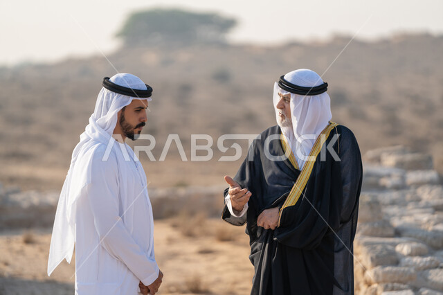 ارتداء الازياء الشعبية في المناسبات الوطنية، تبادل الاحاديث وزيارة الاماكن التاريخية، اليوم الوطني الاماراتي 1971، تأسيس الاتحاد 2 ديسمبر، شاب عربي خليجي إماراتي يرتدي الكندورة والغترة يتجول مع رجل يرتدي البشت في منطقة أثرية في الصحراء، الفخر والاعتزاز وحب الوطن