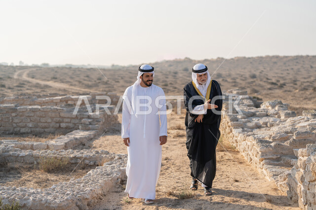 المشي وتبادل الاحاديث في الاماكن التاريخية، اليوم الوطني الاماراتي 1971، تأسيس الاتحاد 2 ديسمبر، شاب عربي خليجي إماراتي يرتدي الكندورة والغترة يتجول مع رجل يرتدي البشت في الصحراء، الفخر والاعتزاز وحب الوطن، ارتداء الازياء الشعبية في المناسبات الوطنية