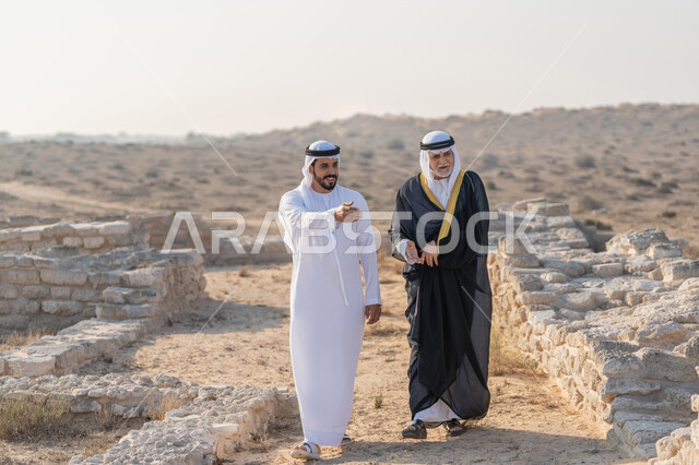 التجول وتبادل الاحاديث في الاماكن التاريخية، اليوم الوطني الاماراتي 1971، تأسيس الاتحاد 2 ديسمبر، شاب عربي خليجي إماراتي يرتدي الكندورة والغترة يتجول مع رجل يرتدي البشت في الصحراء، الفخر والاعتزاز وحب الوطن، ارتداء الازياء الشعبية في المناسبات الوطنية