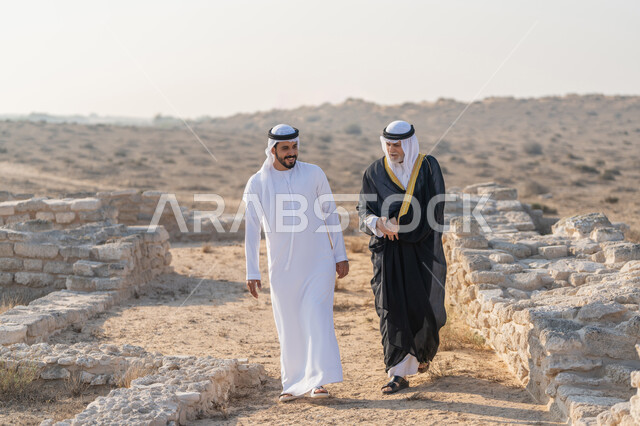 المشي وتبادل الاحاديث في الاماكن التاريخية، اليوم الوطني الاماراتي 1971، تأسيس الاتحاد 2 ديسمبر، شاب عربي خليجي إماراتي يرتدي الكندورة والغترة يتجول مع رجل يرتدي البشت في الصحراء، الفخر والاعتزاز وحب الوطن، ارتداء الازياء الشعبية في المناسبات الوطنية
