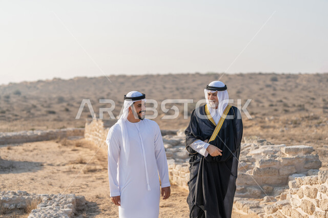 المشي وتبادل الاحاديث في الاماكن التاريخية، اليوم الوطني الاماراتي 1971، تأسيس الاتحاد 2 ديسمبر، شاب عربي خليجي إماراتي يرتدي الكندورة والغترة يتجول مع رجل يرتدي البشت في الصحراء، الفخر والاعتزاز وحب الوطن، ارتداء الازياء الشعبية في المناسبات الوطنية