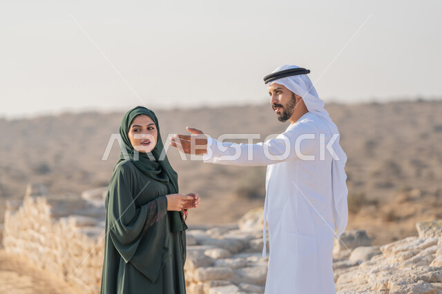 اليوم الوطني الاماراتي 1971، تأسيس الاتحاد 2 ديسمبر، شاب عربي خليجي إماراتي يرتدي الكندورة والغترة يتجول مع إمراة ترتدي العباءة والحجاب في منطقة أثرية في الصحراء، تعابير وايماءات الفخر والاعتزاز وحب الوطن، تبادل الاحاديث وزيارة الاماكن التاريخية القديمة